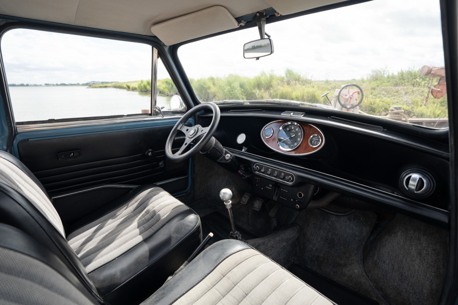 Interior view of a classic car, featuring a dashboard, steering wheel, and textured seats against a scenic backdrop.