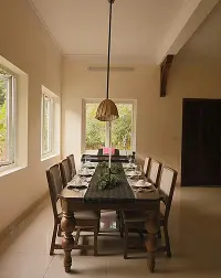 Warm minimalist dining room with long wood table, pendant light, and tall windows