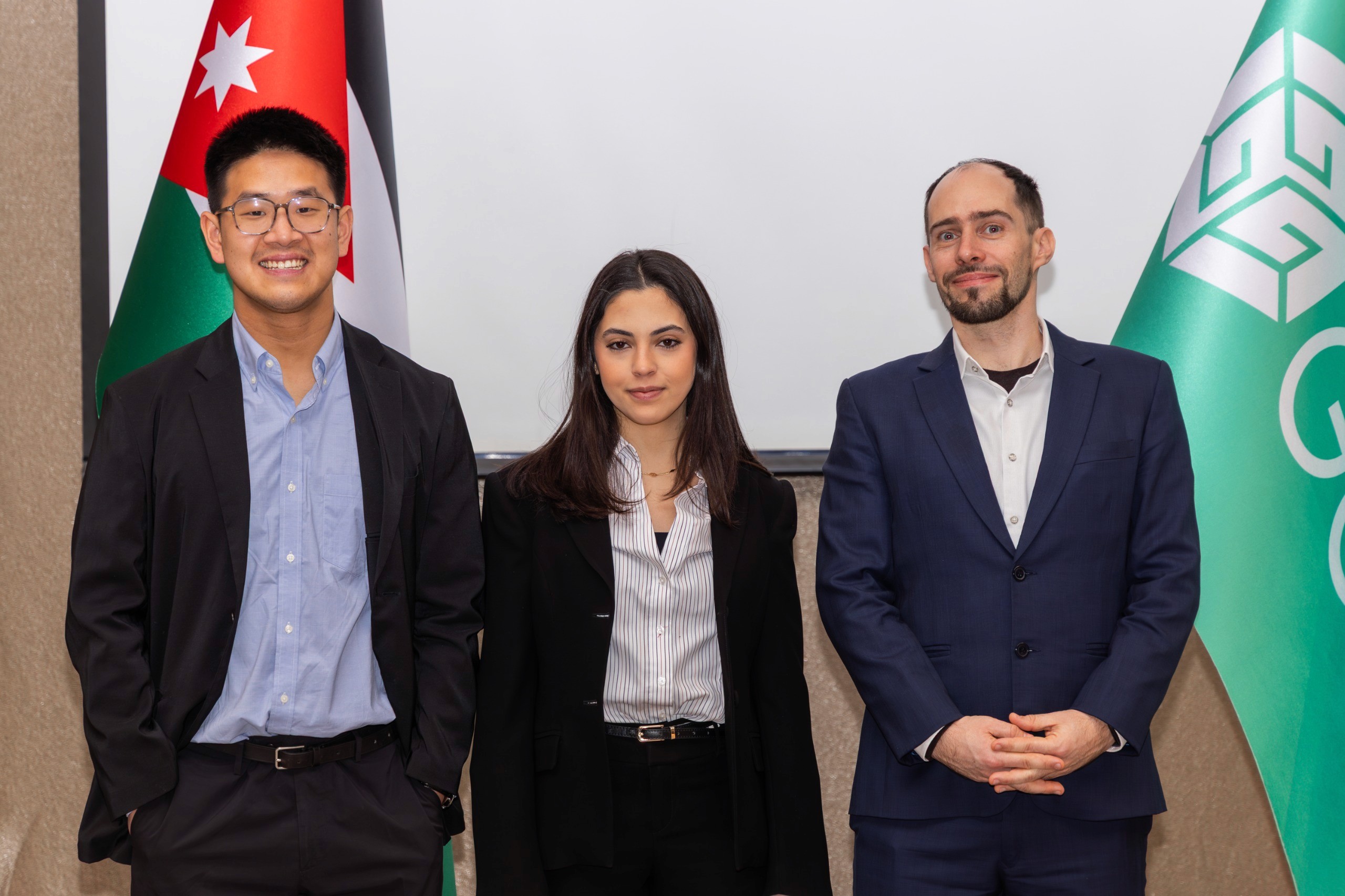 Three development professionals standing between Jordanian and international flags
