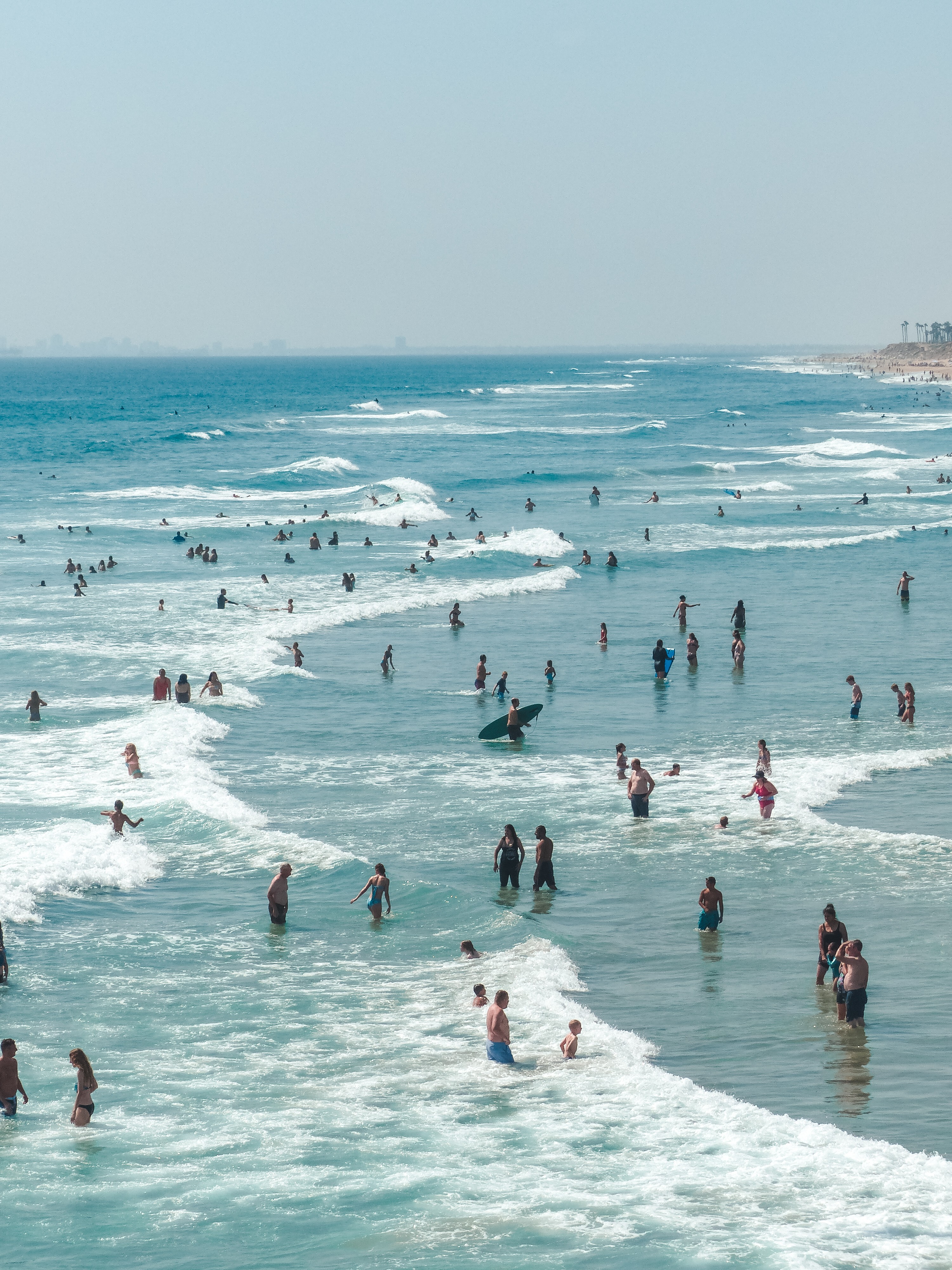 Plage fréquentée avec baigneurs debout dans l’eau – ambiance estivale et lifestyle bord de mer