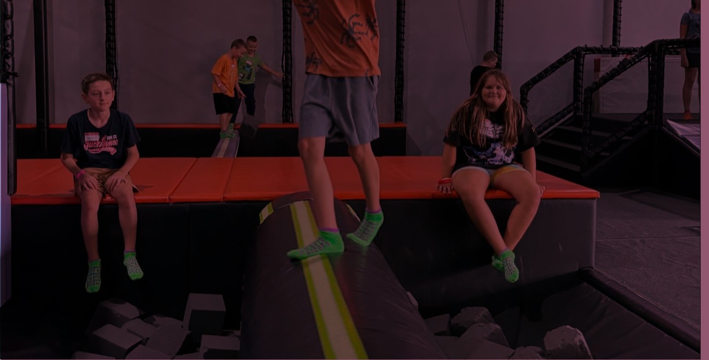 girl smiling jumping on trempolines wearing pink tishirt, grey pants and orange ABS socks