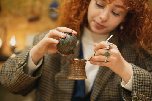 A person crafting a Turkish mosaic lamp, carefully applying multicolored beads to the ornament. The background shows a workshop setting with tools hanging on the wall.