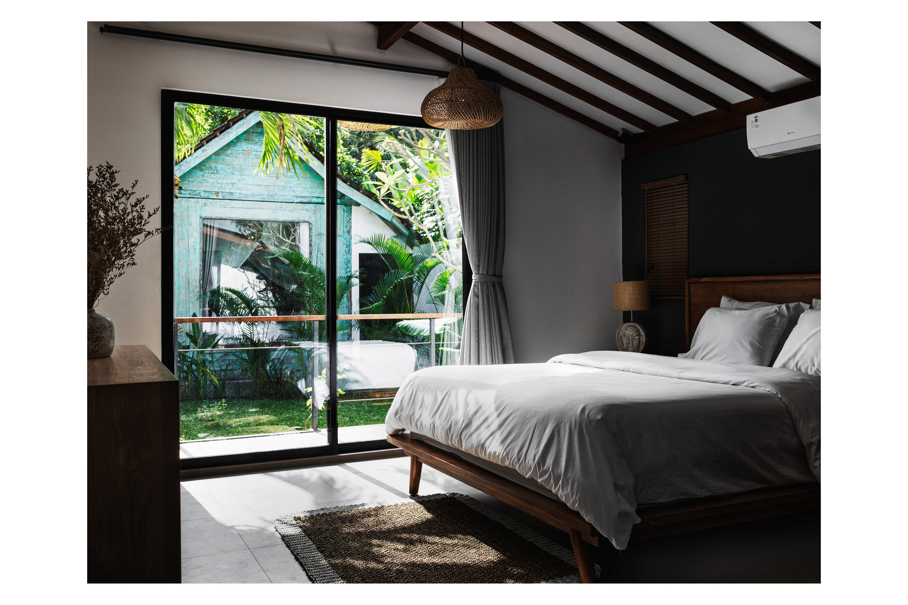 Light-filled bedroom with pitched ceiling, rattan pendant light, and garden view through floor-to-ceiling glass doors.