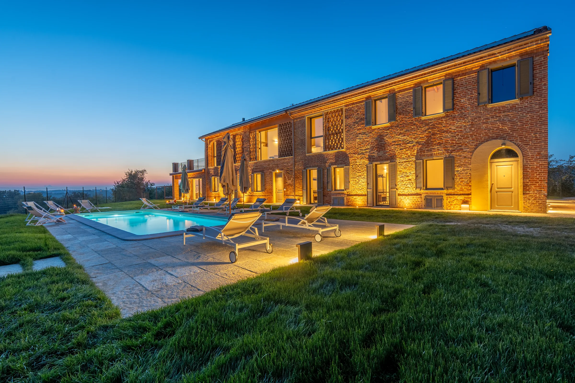 Brick villa and swimming pool at blue hour in Fubine Monferrato, Italy. Photography by Yunes Calore.