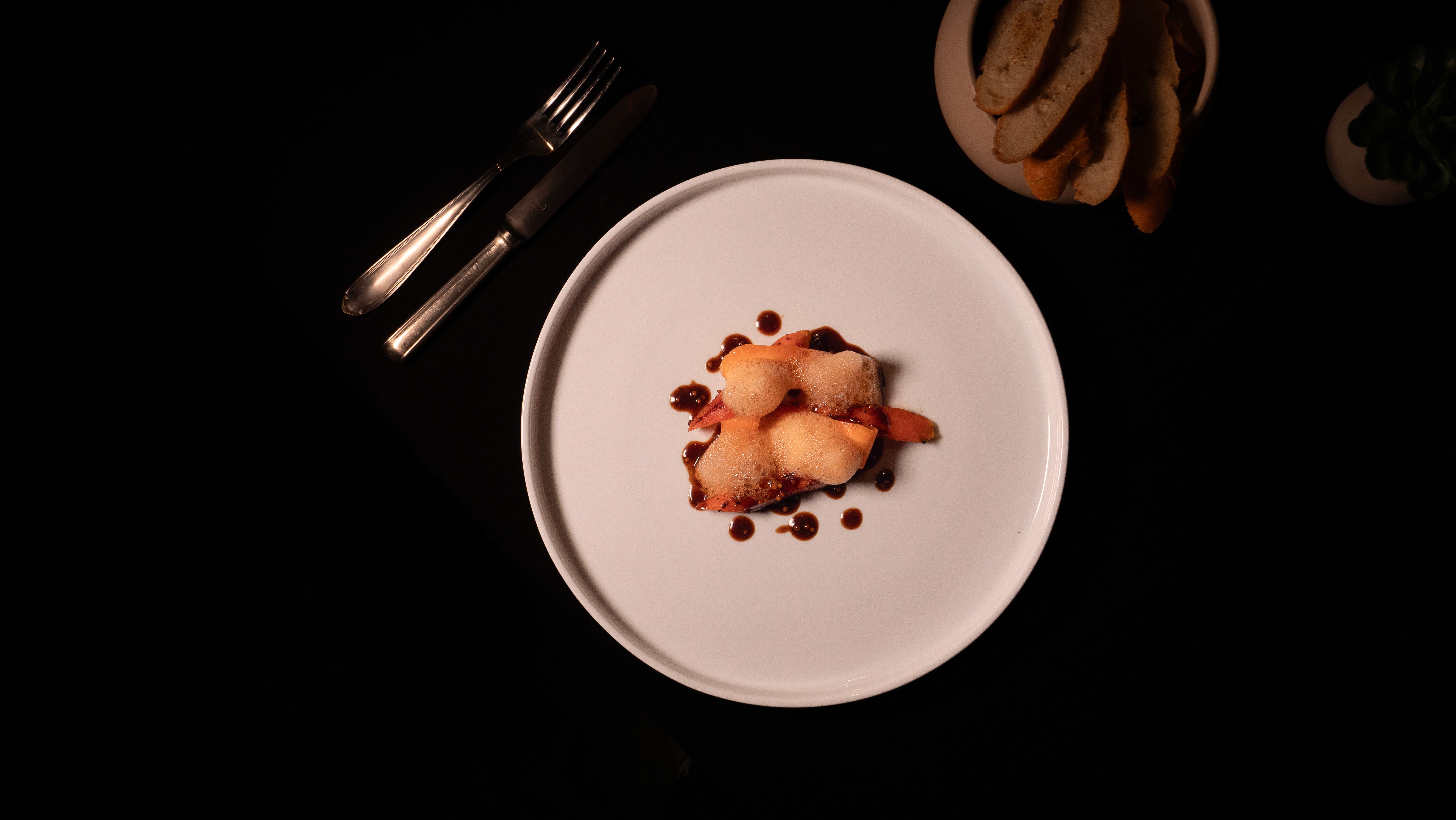 Restaurant interior with wooden tables and chairs lined against a textured wall, softly lit by round wall lamps.