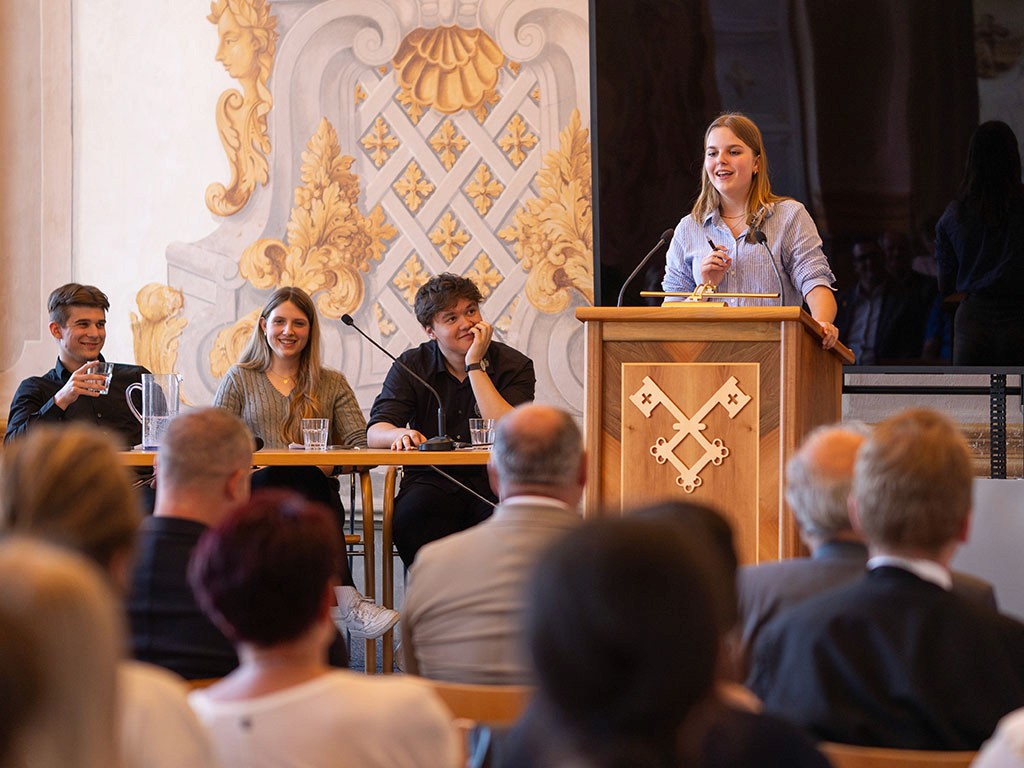  Eröffnungsrede bei der Debattenschmiede – junge Rednerin spricht strukturiert vor Schülerpublikum.
