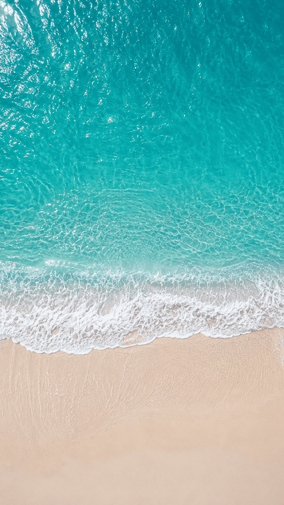 Top-down view of clear blue ocean waves on a clean sandy shore, showcasing the coastal environment near Barcelona.