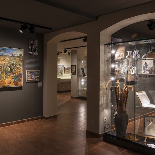 一个博物馆展览,墙上挂满了画作,文物则在柔和灯光下的玻璃柜中展出。