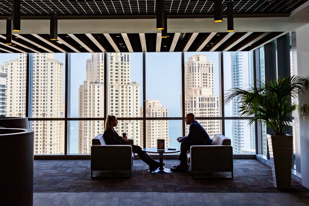 Two professionals talking in the myOffice lounge against the Dubai skyscrapers.&nbsp;