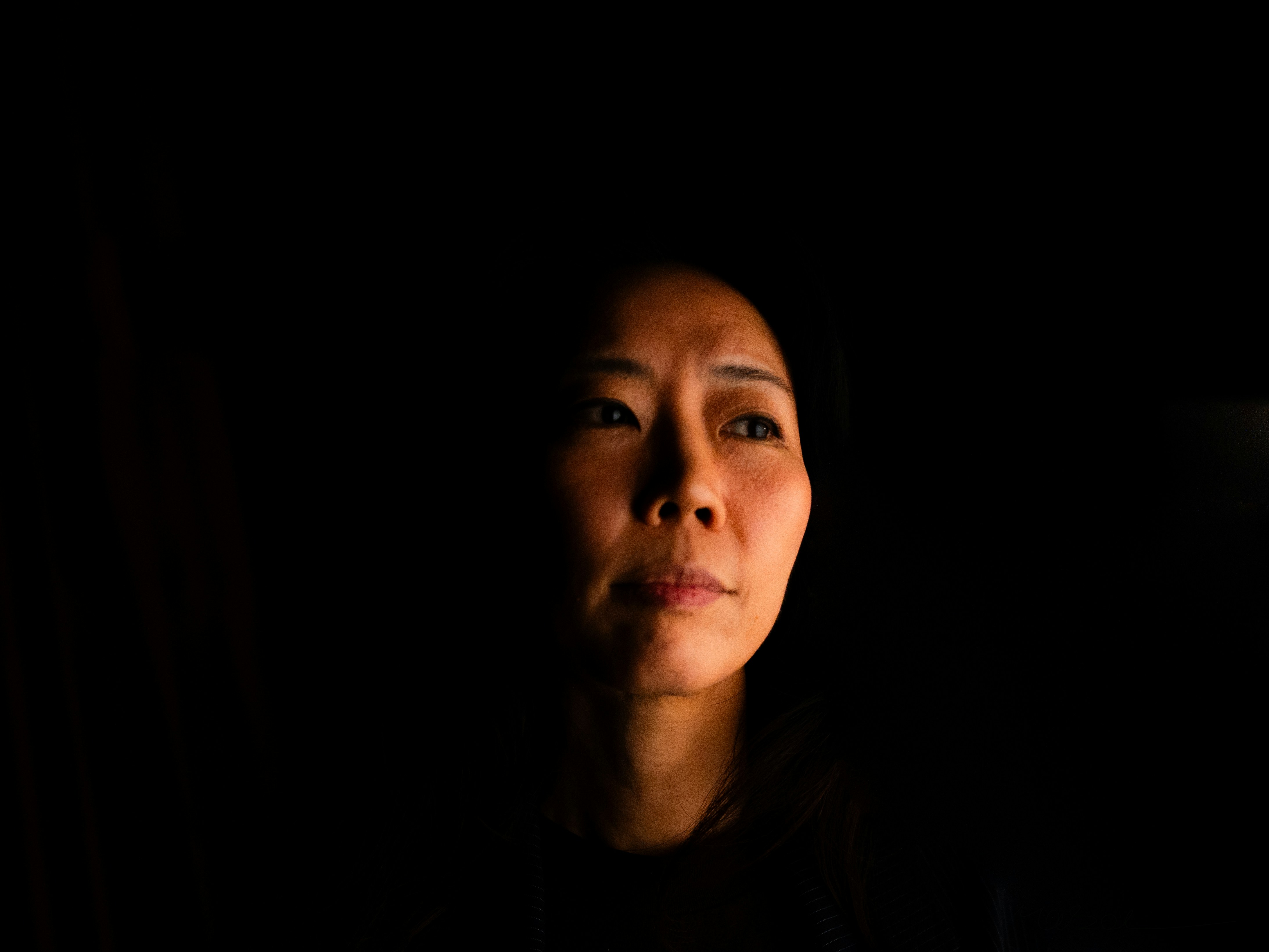 Woman's face illuminated by dim light against darkness