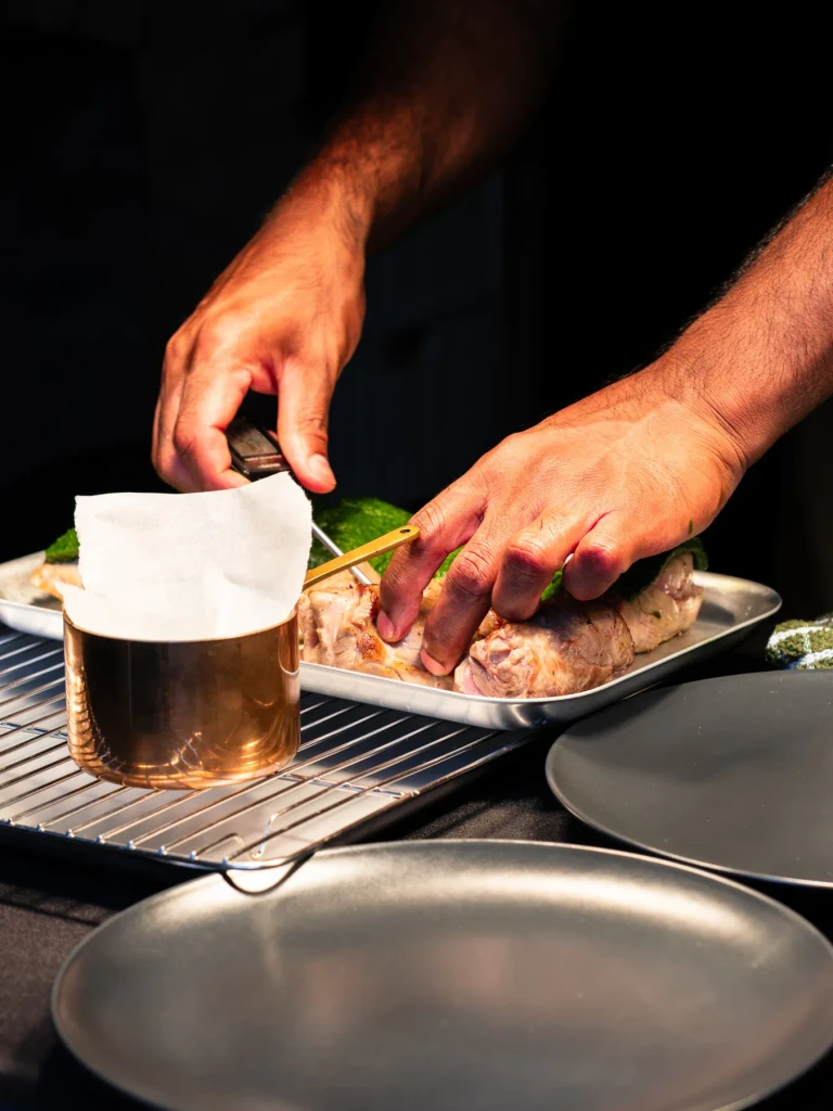 Josh checking herb crusted Herdwick lamb beside a copper pan
