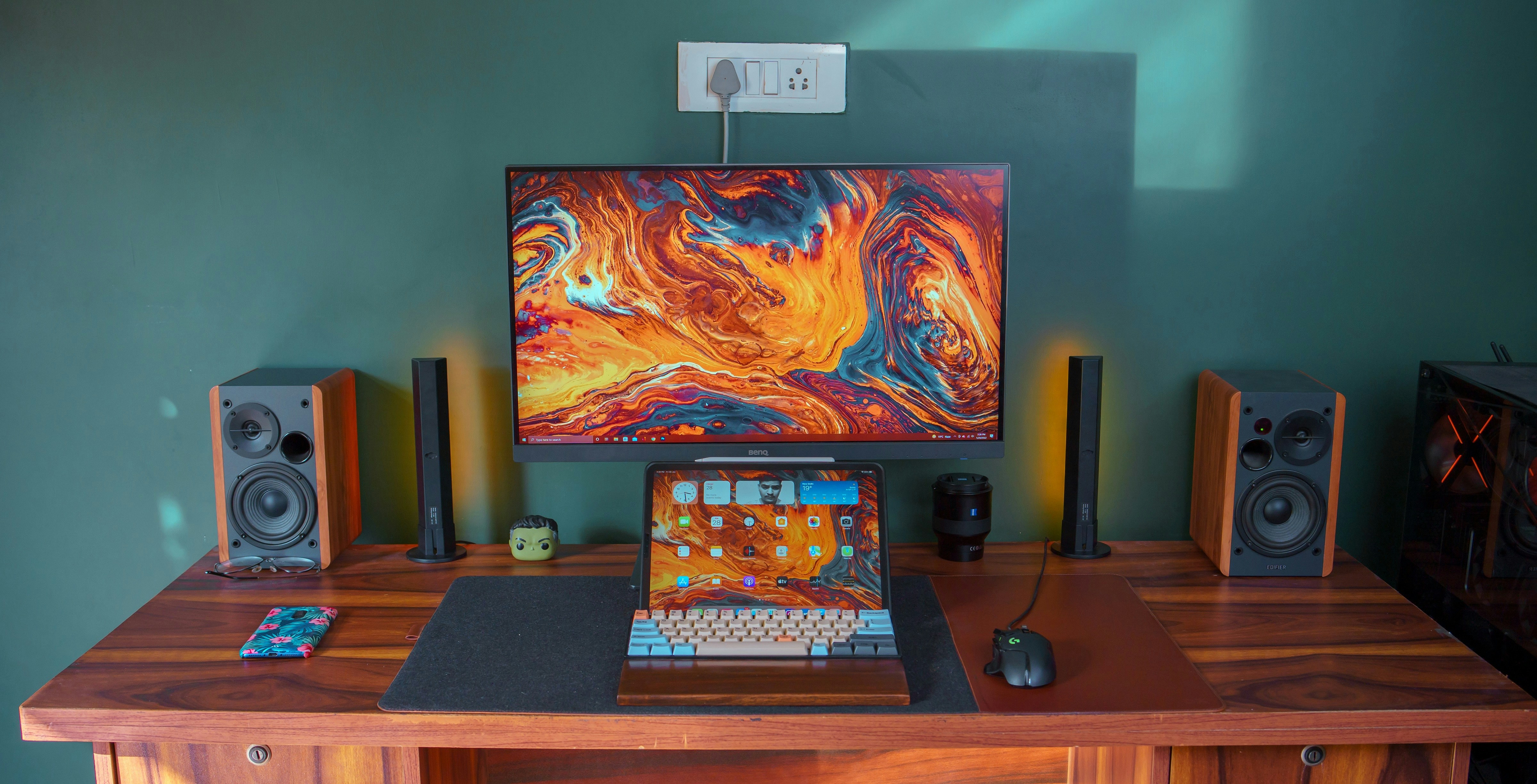 an iPad on a desk with a p3 monitor behind it as well as desktop speakers and a mechanical keyboard and a gaming mouse
