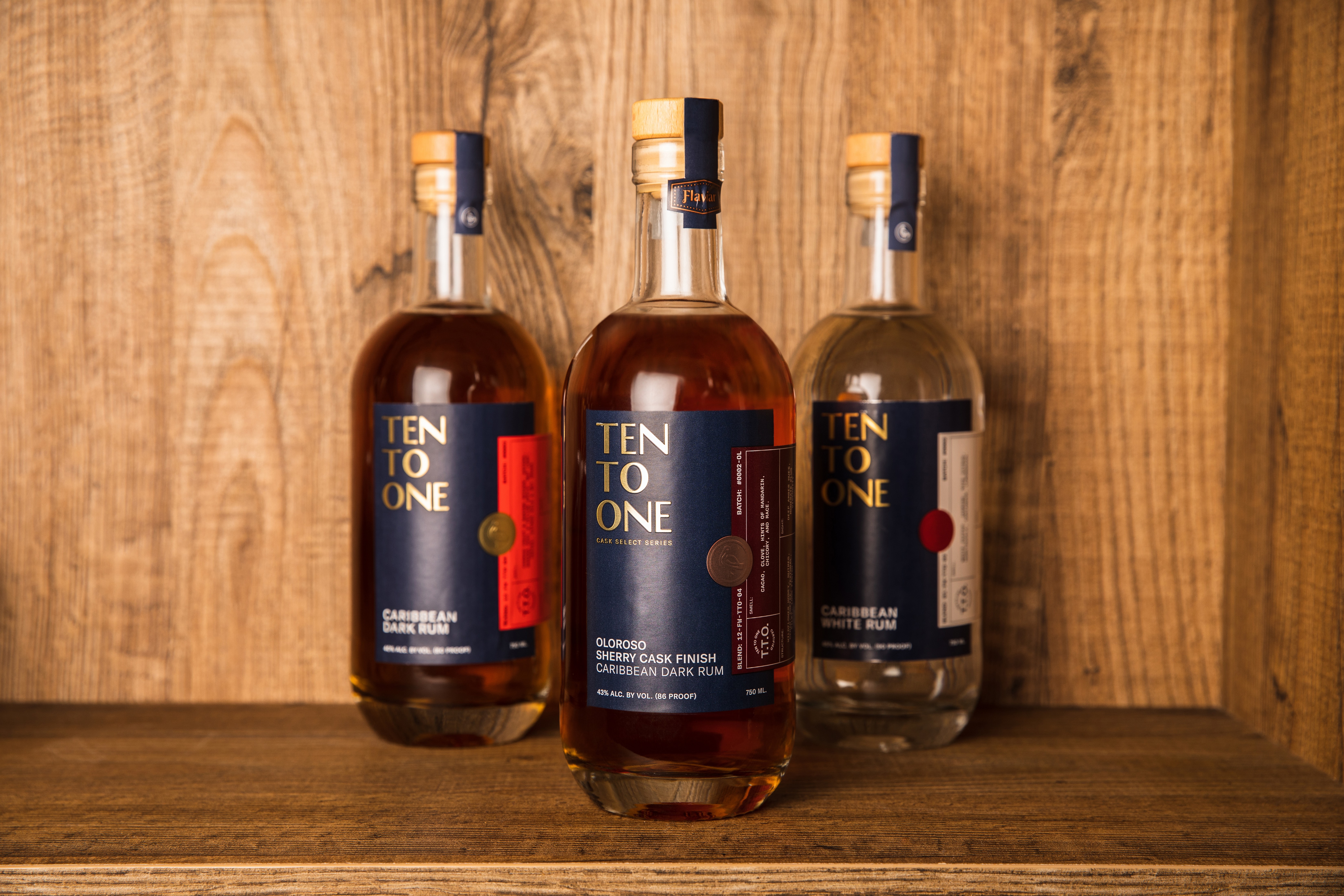 Three Ten To One rum bottles arranged on a wooden shelf against a wood backdrop.