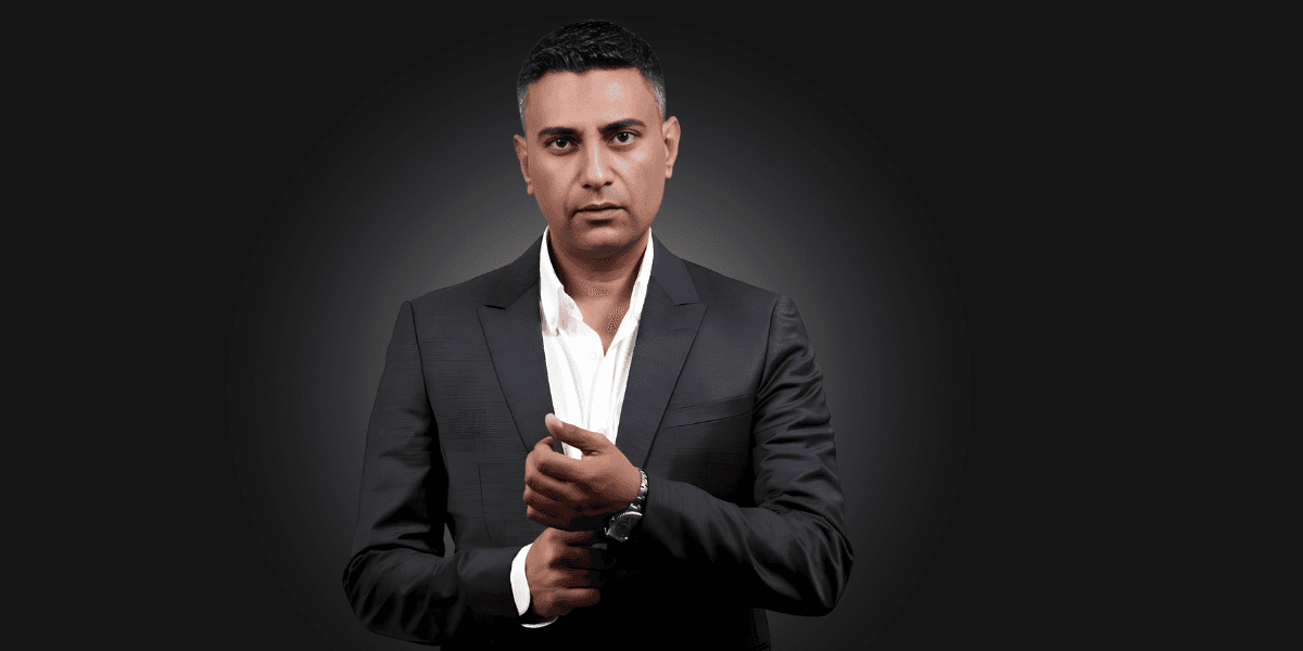 Mohamed El Mahdy in a dark suit, adjusting his cuff, posing confidently against a dark gradient background.