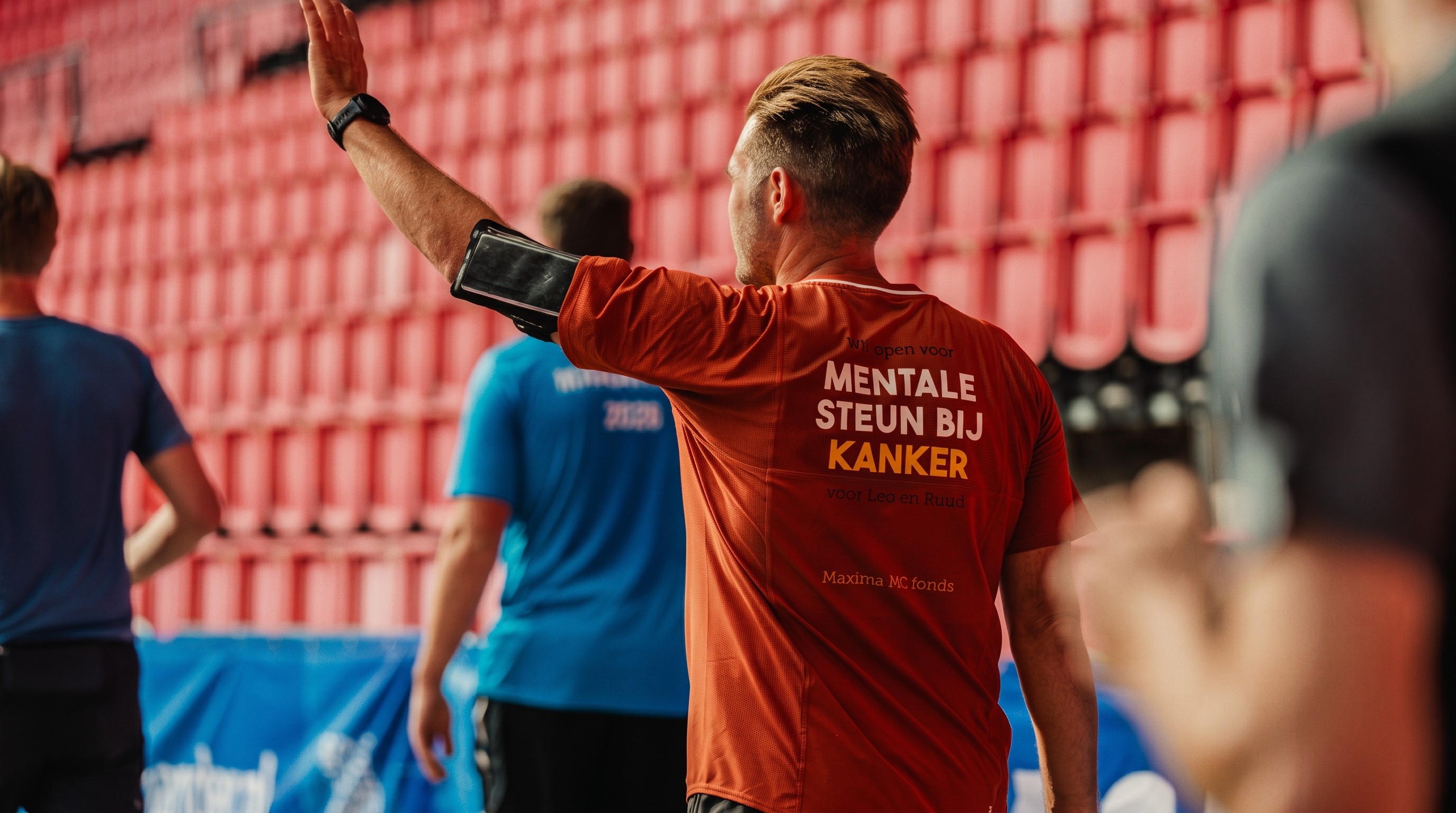 Trainer in oranje shirt geeft met opgestoken arm een teken in een stadion