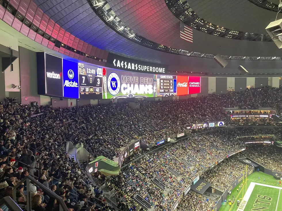 Crowd-filled Caesars Superdome during an NFL game with illuminated sponsorship signage from brands like Verizon, Allstate, and Coca-Cola visible across the stadium interior.
