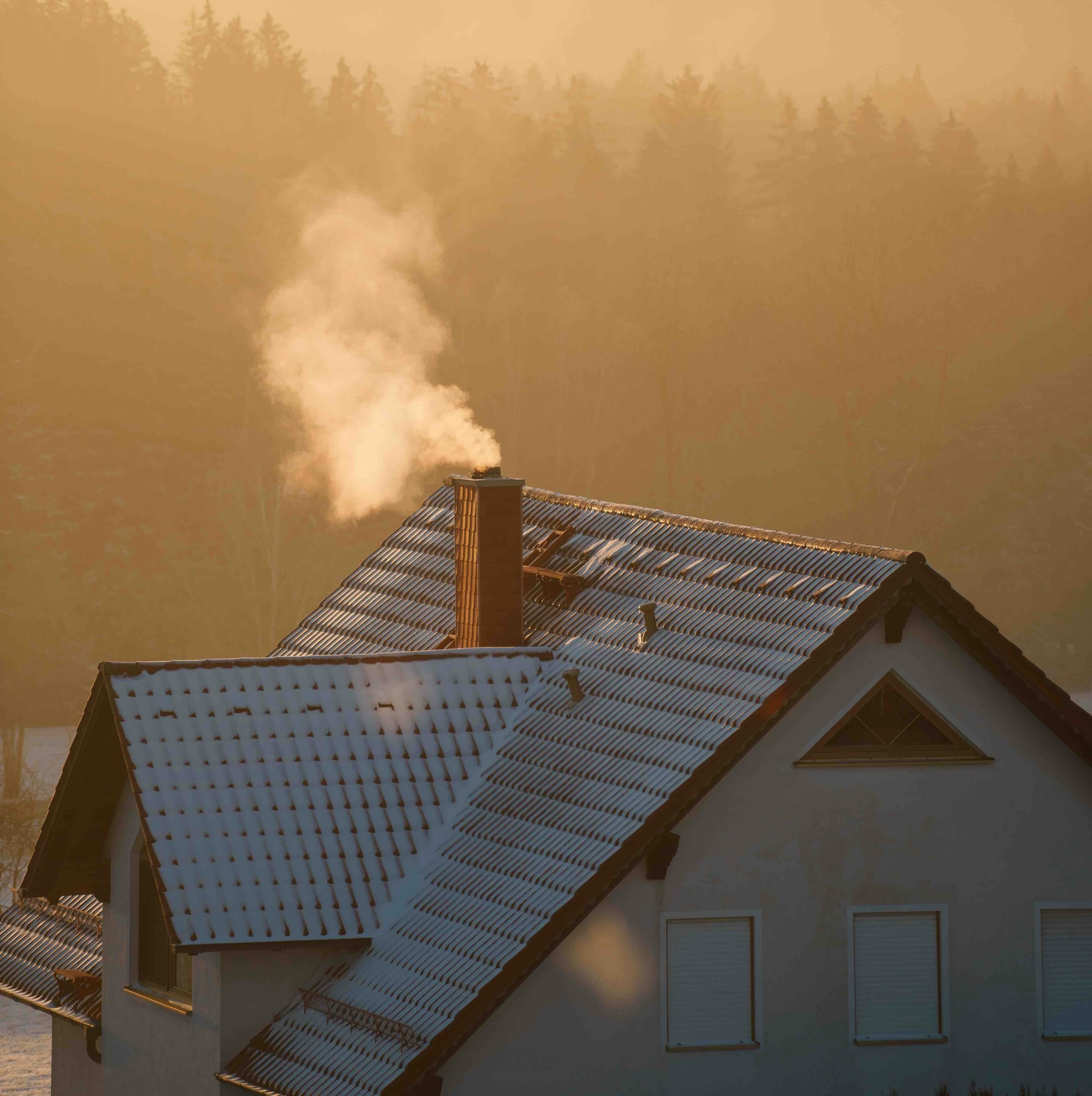 House rooftop with chimney smoke in foggy conditions, illustrating thermal efficiency of Strawtown straw building panels