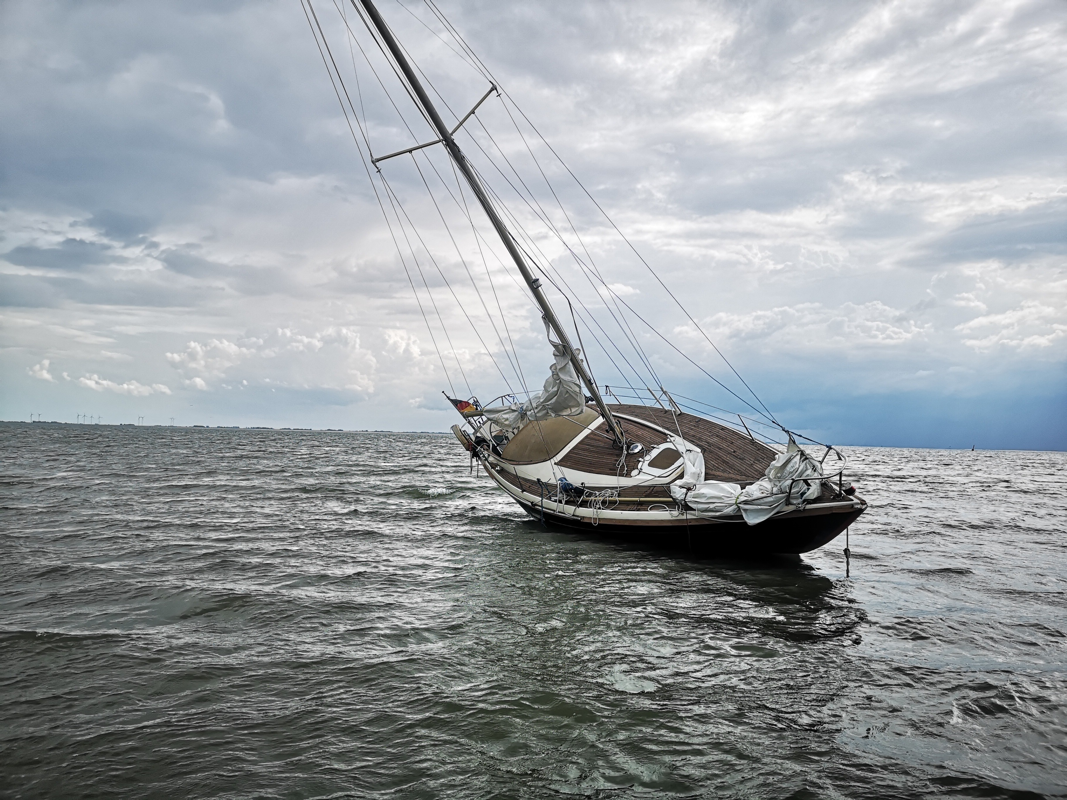 Sailboat listing to one side in rough choppy water under storm clouds.