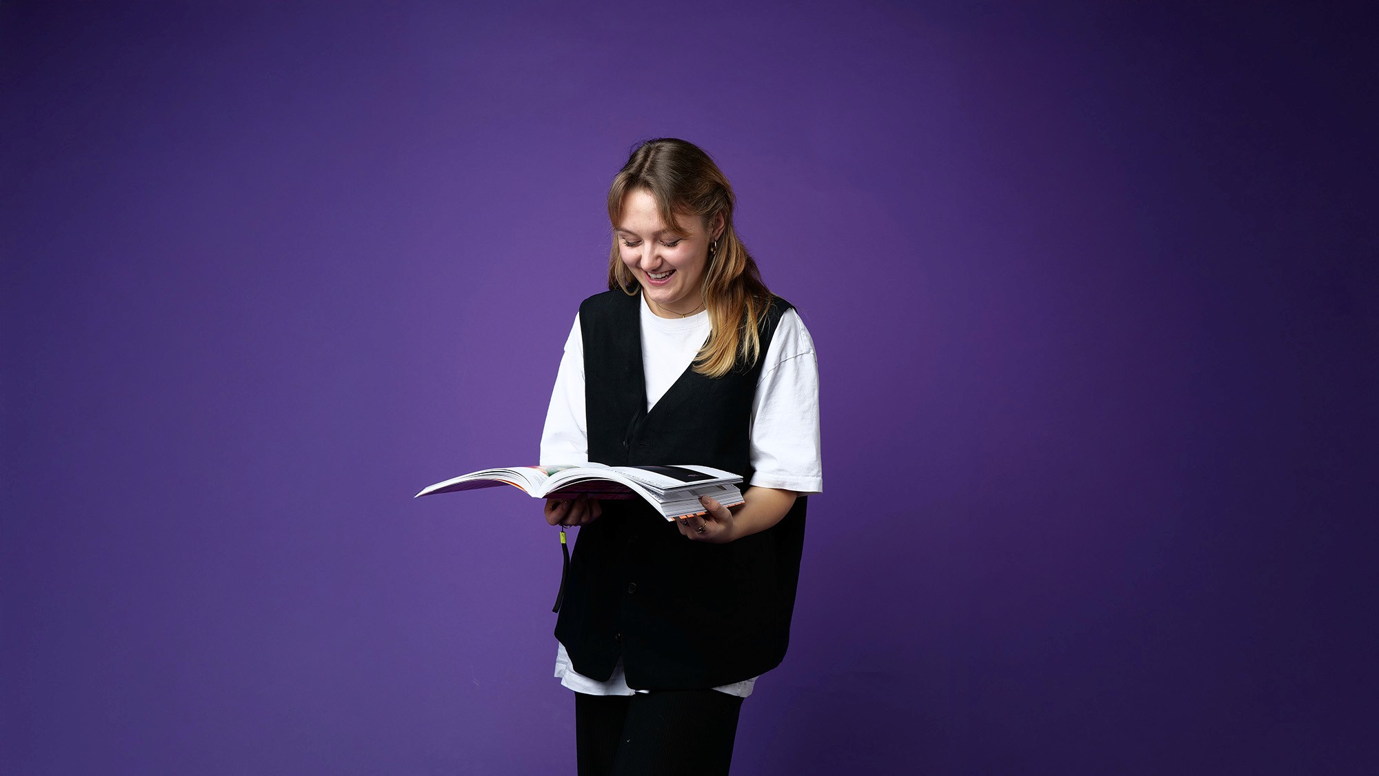 Modern minimalist desk setup with a computer monitor, microphone arm, camera, and indoor plants, featuring a pegboard with accessories on the wall and a Bauhaus-style poster leaning against the wall.