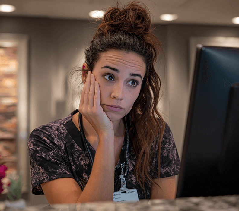 A MedSpa receptionist at her desk looking stressed while checking messages and missed calls. The image illustrates slow lead follow-up and potential revenue leaks that ClinicROI helps identify and measure.