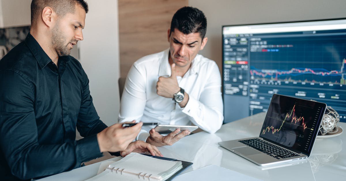Two professionals discuss data analysis on digital devices in an office setting, focusing on graphs