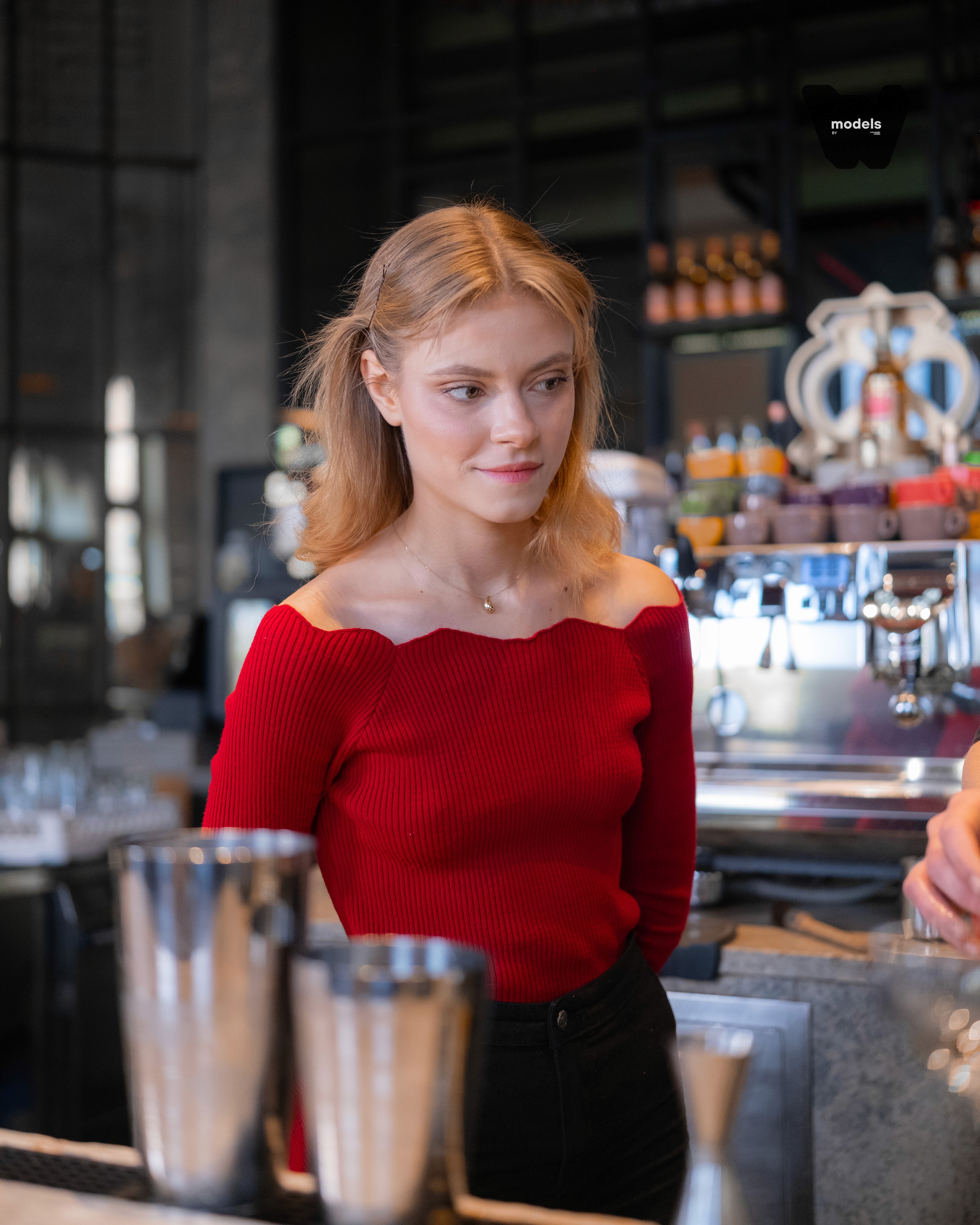 A smiling young man with crossed arms, wearing a plaid shirt and white t-shirt, poses against a dark background.