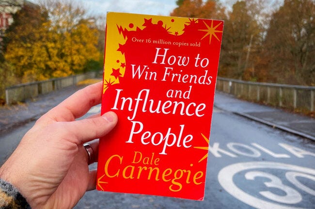 How To Win Friends and Influence People book being held by one hand.
