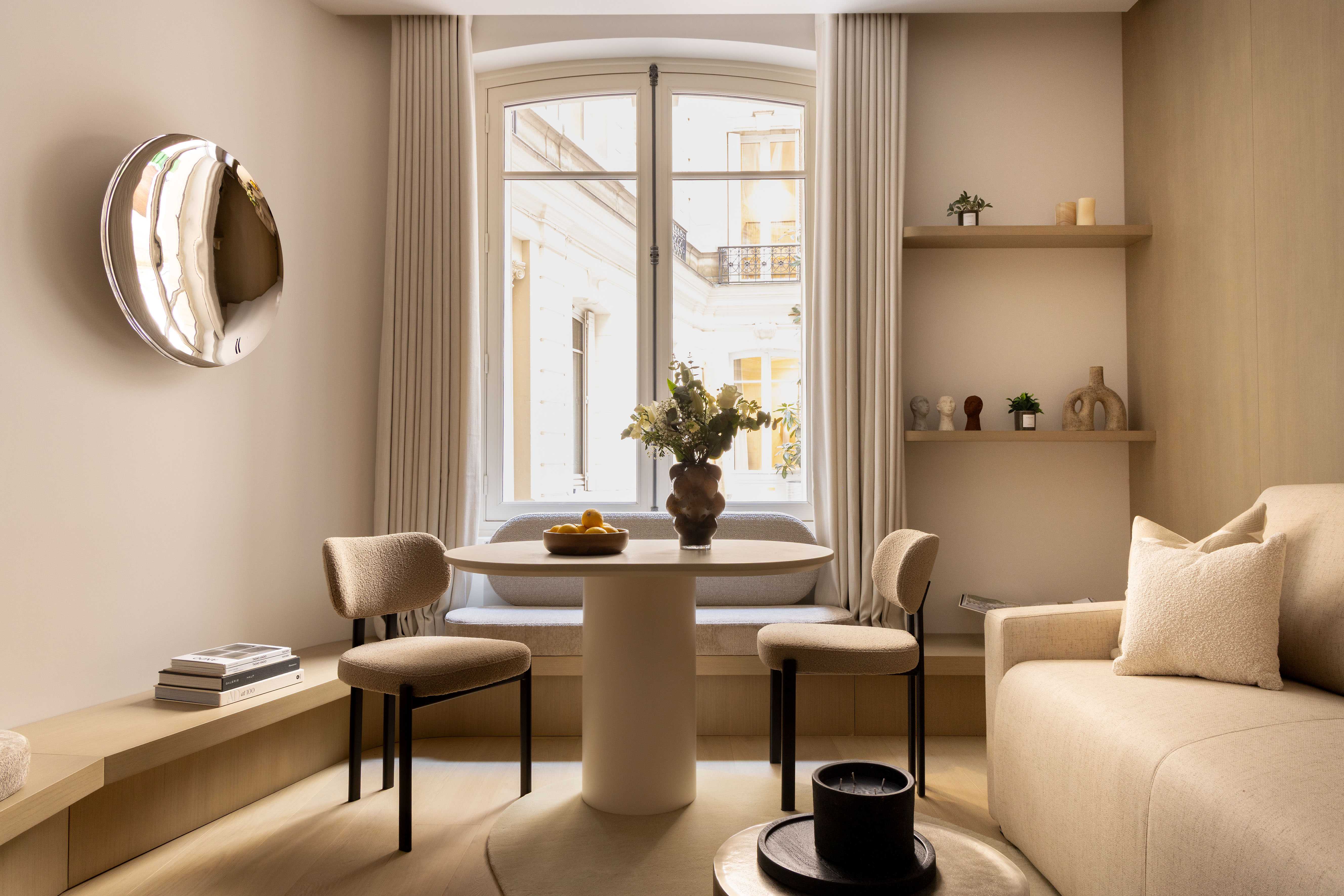 Coin repas avec table ronde blanche, chaises et applique murale design, vue sur cour parisienne