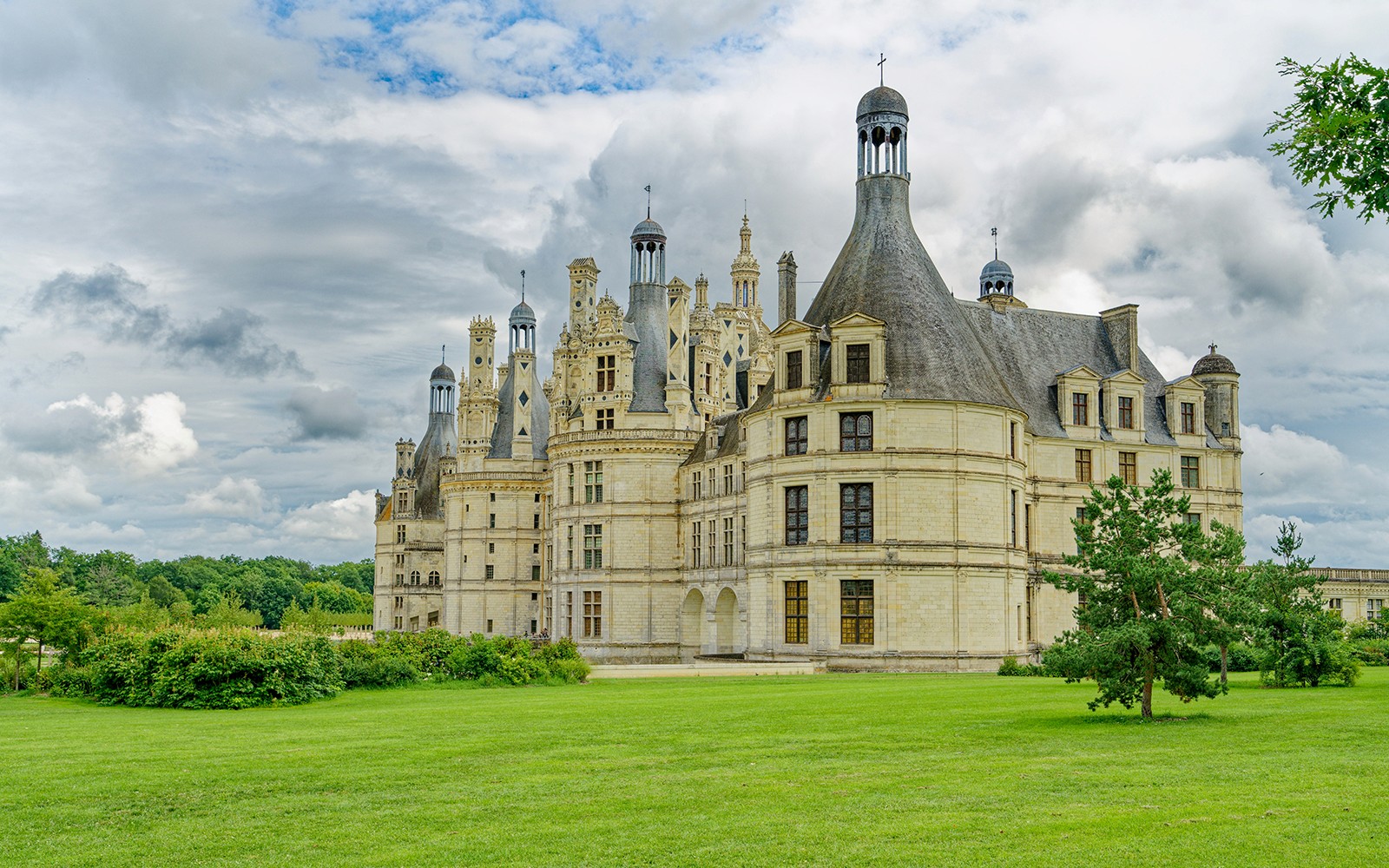 Château de Chambord con terrenos verdes exuberantes bajo un cielo nublado, parte del tour Chambord y Chenonceau.