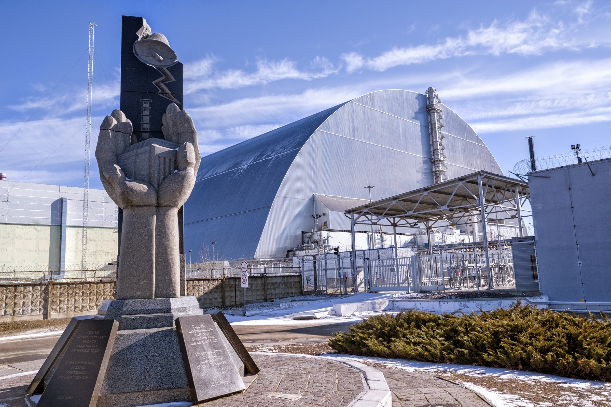 Monument to the Chernobyl liquidators, with the Chernobyl New Safe Confinement around reactor 4 in the background