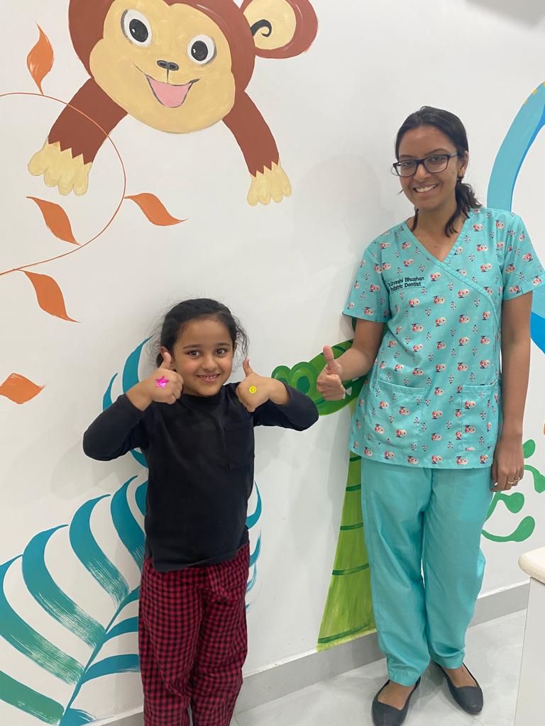 Dr. Urvashi and a young patient smiling beside the clinic’s animal murals