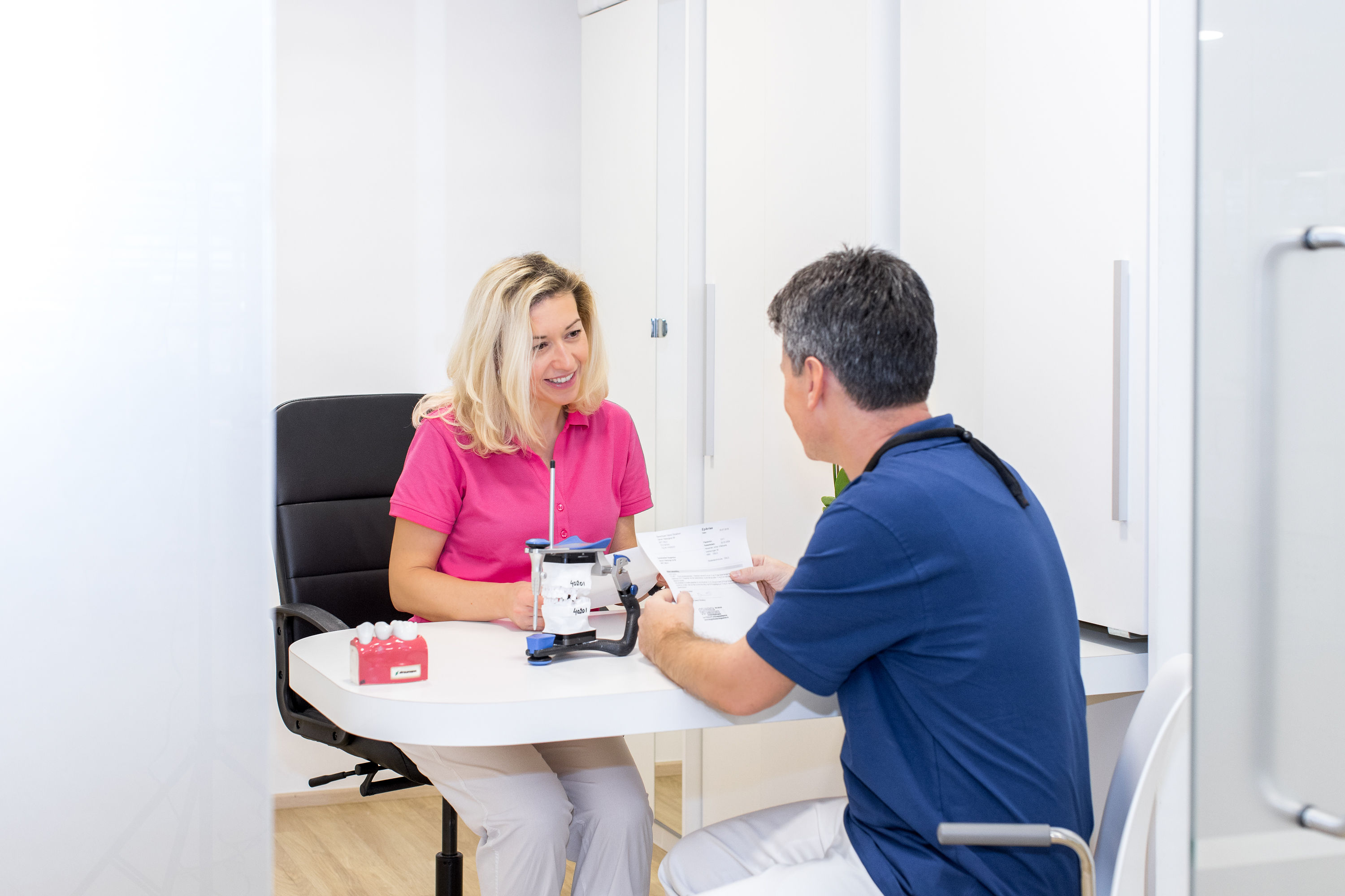 To tannleger ved Haugenstua Tannlegesenter i samtale på kontoret, smilende mens de går gjennom behandlingsplaner og pasientinformasjon.