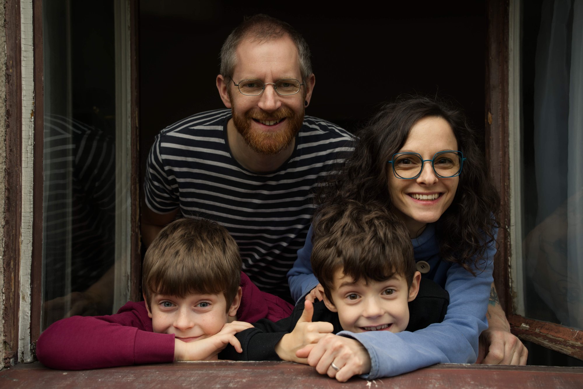 Rodinné focení: tatínek, maminka a dva chlapci se smějí z okna.