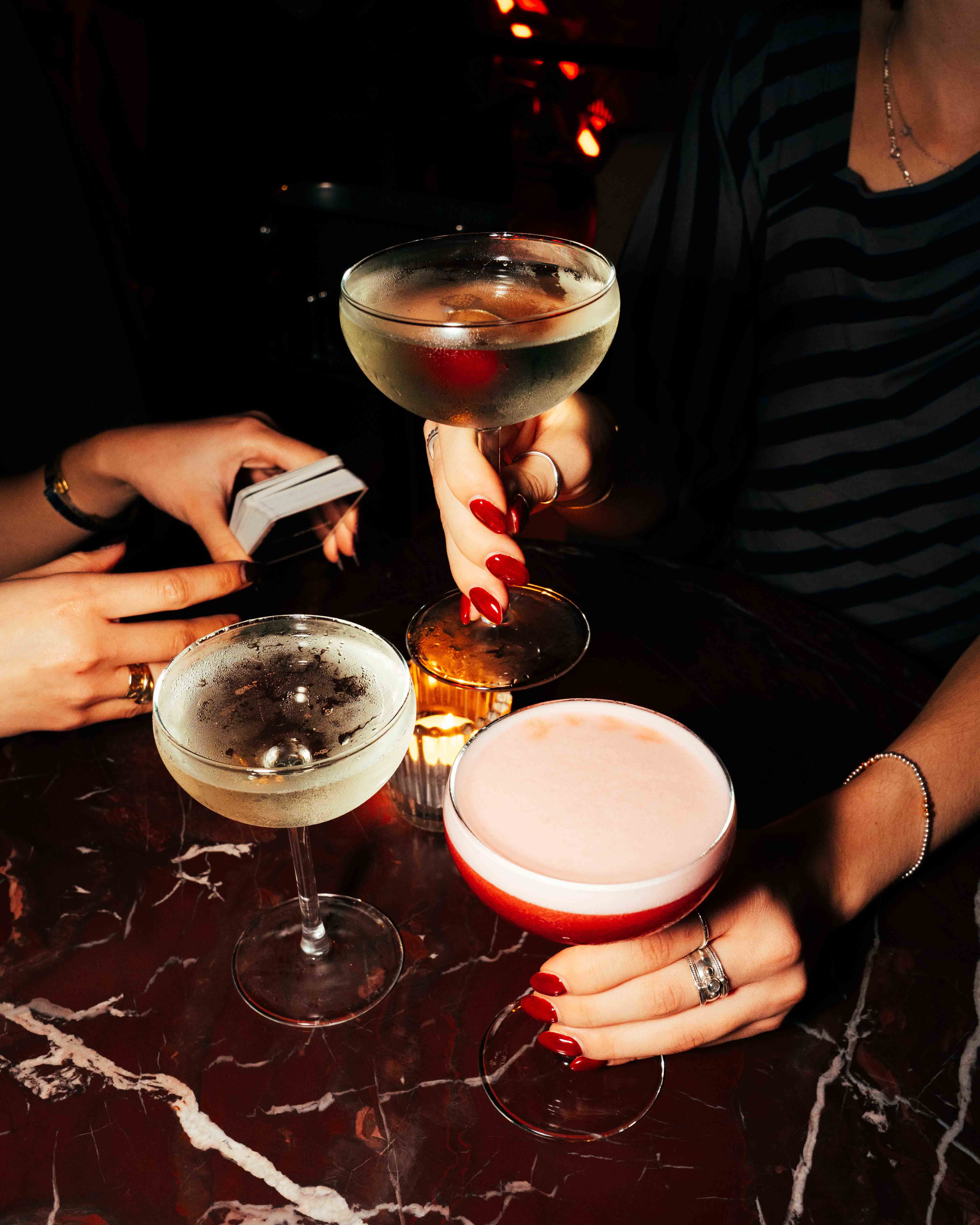 Wooden outdoor table set with multiple plates of food, including dips, salads, potatoes with cheese, and glasses of water, with hands reaching in to eat.