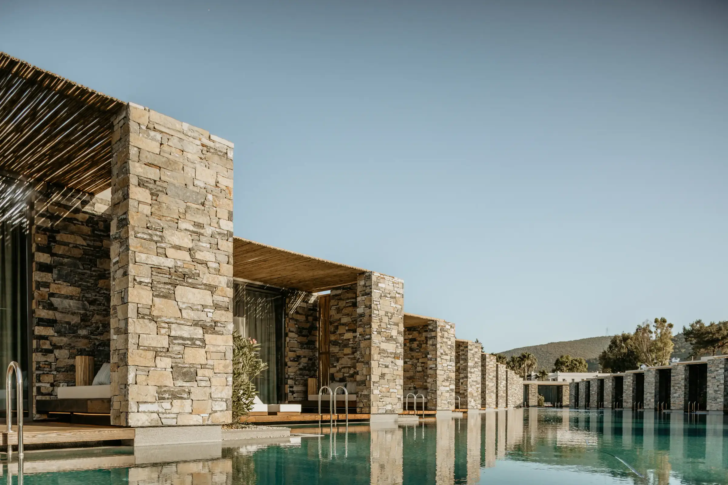 Stone-walled rooms with reed canopies beside the pool