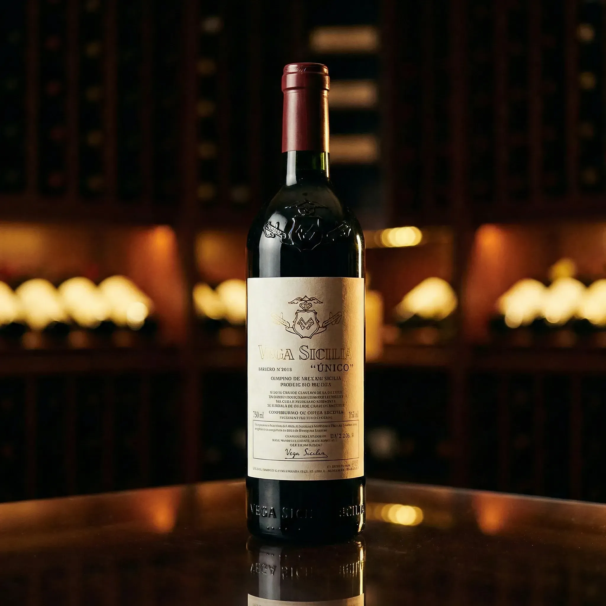 A wine bottle with a red foil top is displayed on a reflective surface in a dimly lit cellar with wooden shelves, creating a warm and luxurious ambiance.