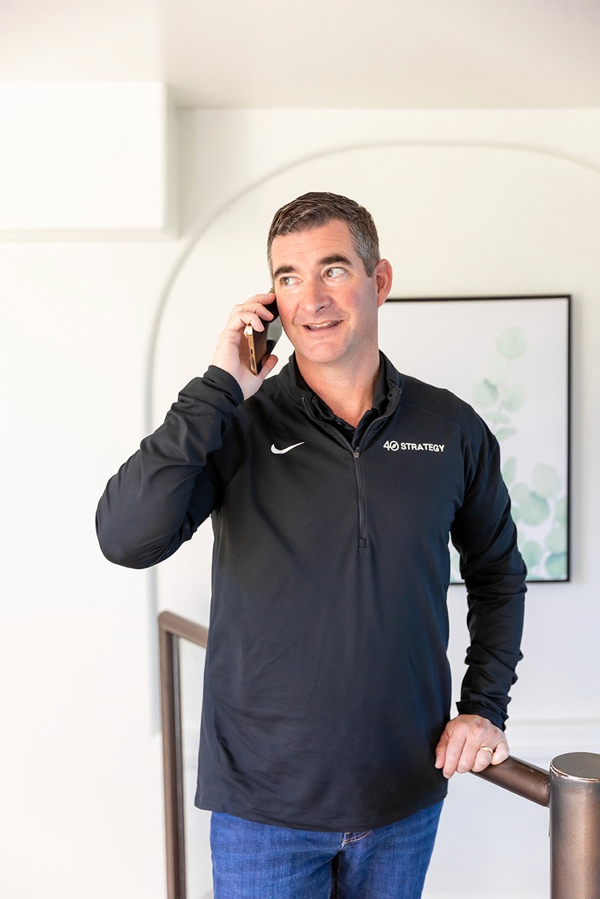 Man in a sweater smiling with arms crossed while standing by a wooden wall.