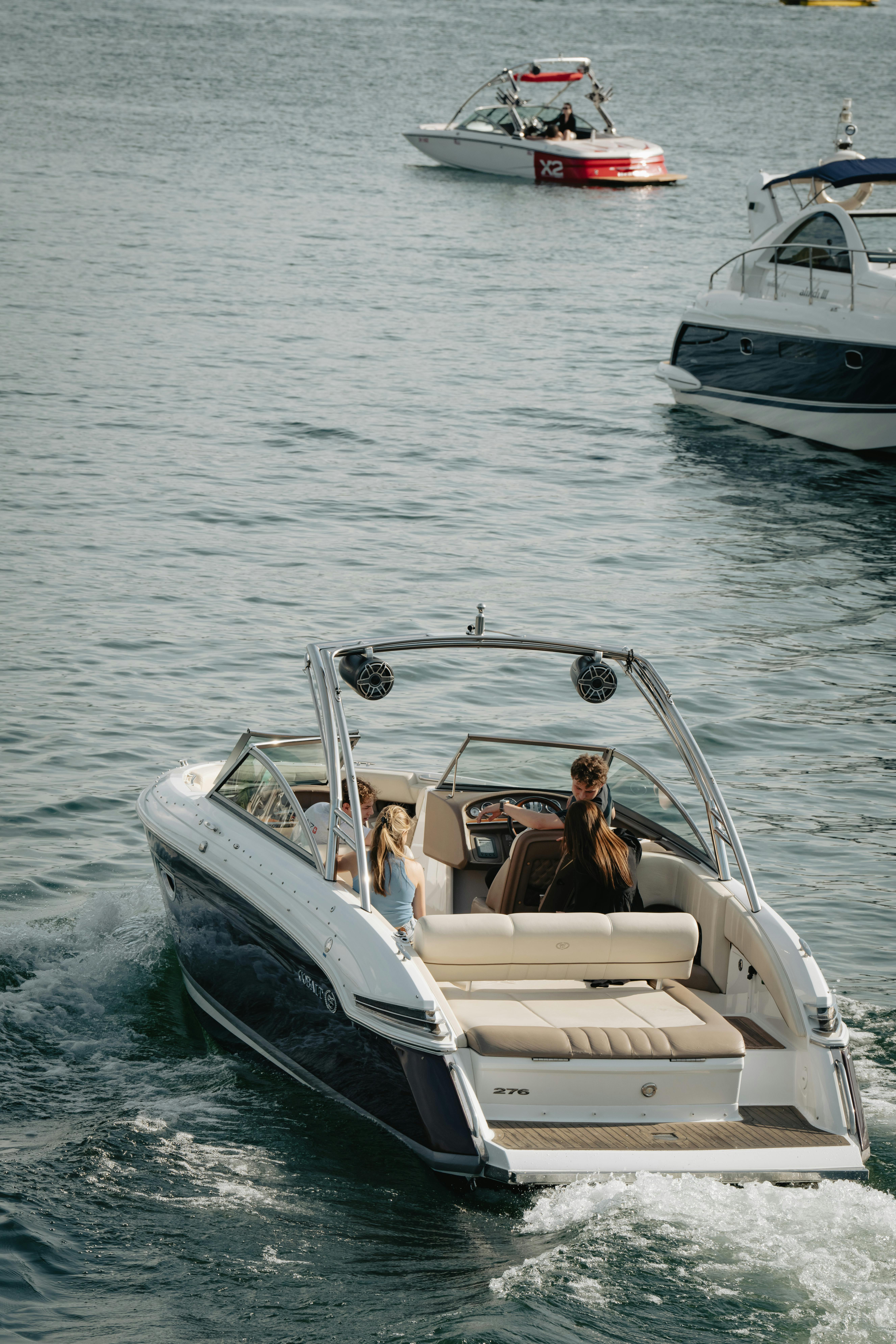 Three stylish motorboats cruise on a serene lake, with one boat in the foreground featuring a sleek design and passengers enjoying a sunny day, highlighting leisure and boating activities.