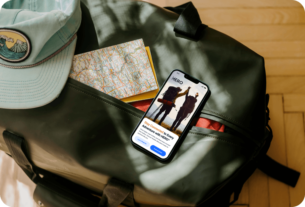 Mobile phone displaying HERO travel app home screen inside an open backpack with travel items.