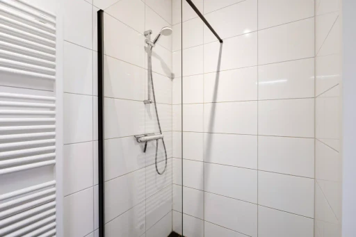 De douchehoek met glazen wand, witte tegels en een zwarte douchevloer.