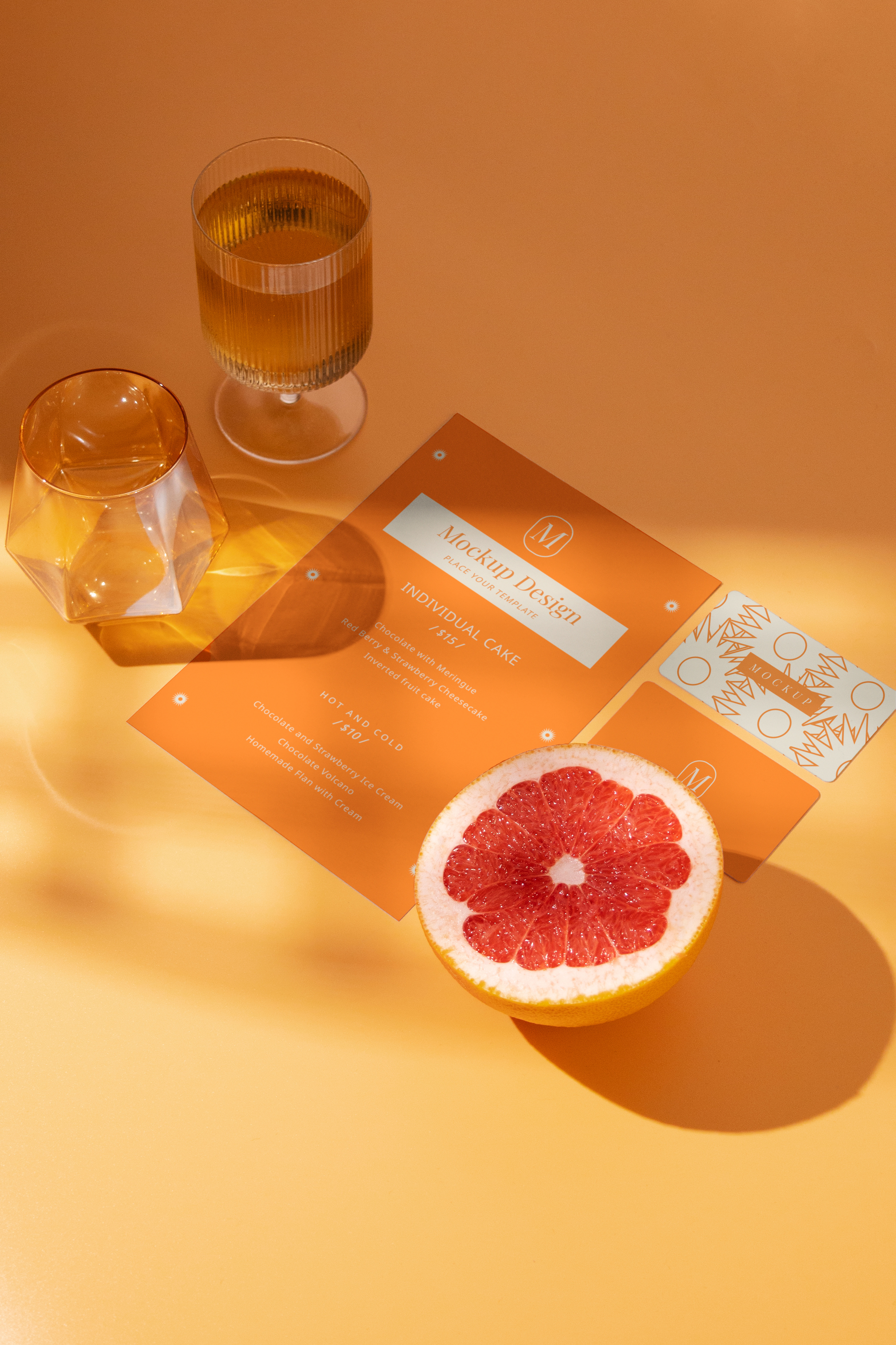 Menu mockup with a grapefruit half and drinks on an orange surface.