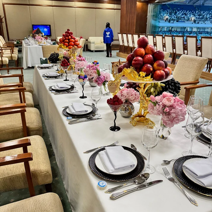 Elegant dining setup with white tablecloths, ornate fruit and flower centerpieces, and formal place settings in a luxurious room.