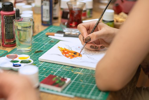 A participant carefully painting a traditional Turkish tile design during a ceramic workshop in Istanbul. The workspace is filled with paint supplies and beverages, emphasizing the hands-on experience of Turkish tile art—a popular attraction in Istanbul.