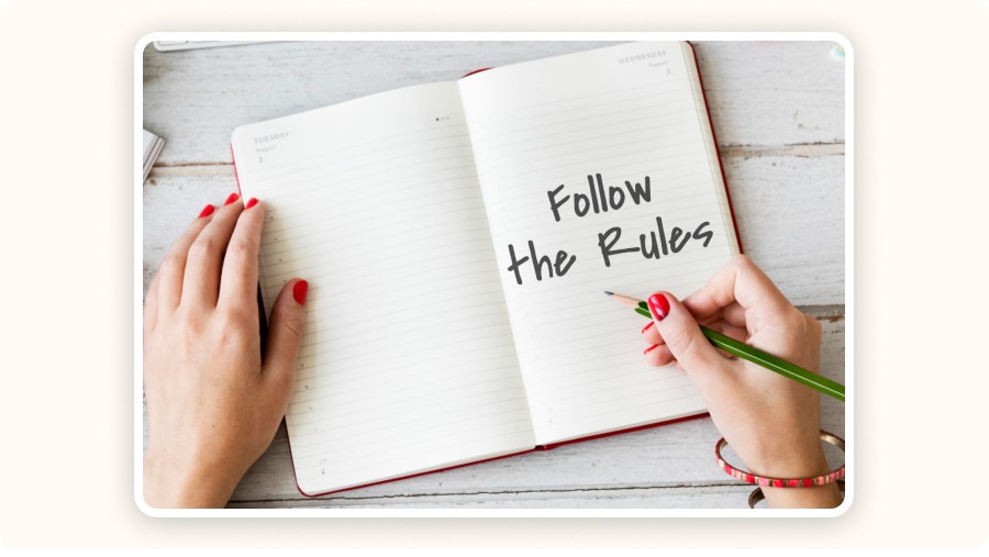 Hands writing “Follow the Rules” inside an open planner notebook