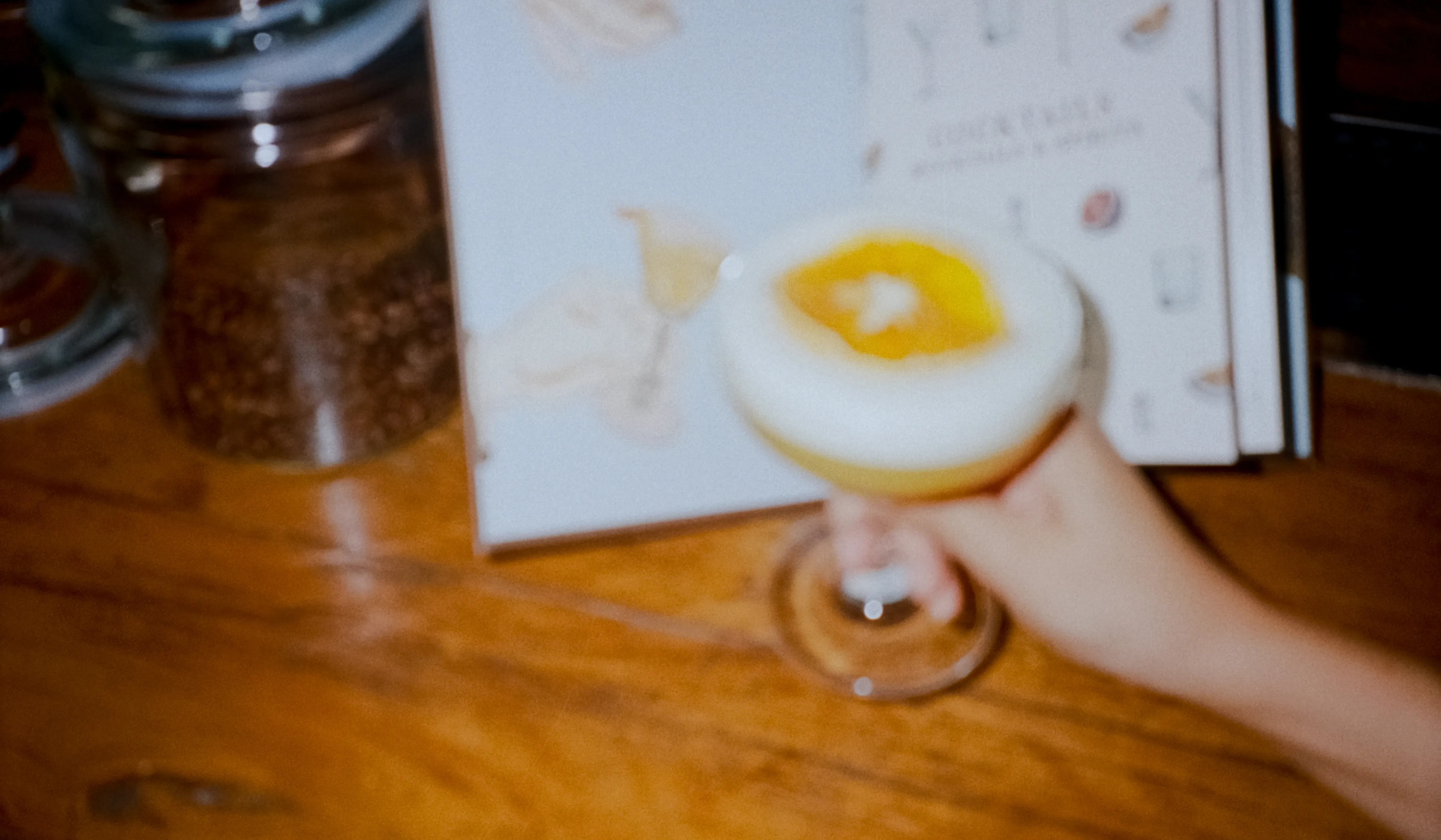 A frothy citrus cocktail on a wooden table, with the Small Bar menu design behind it