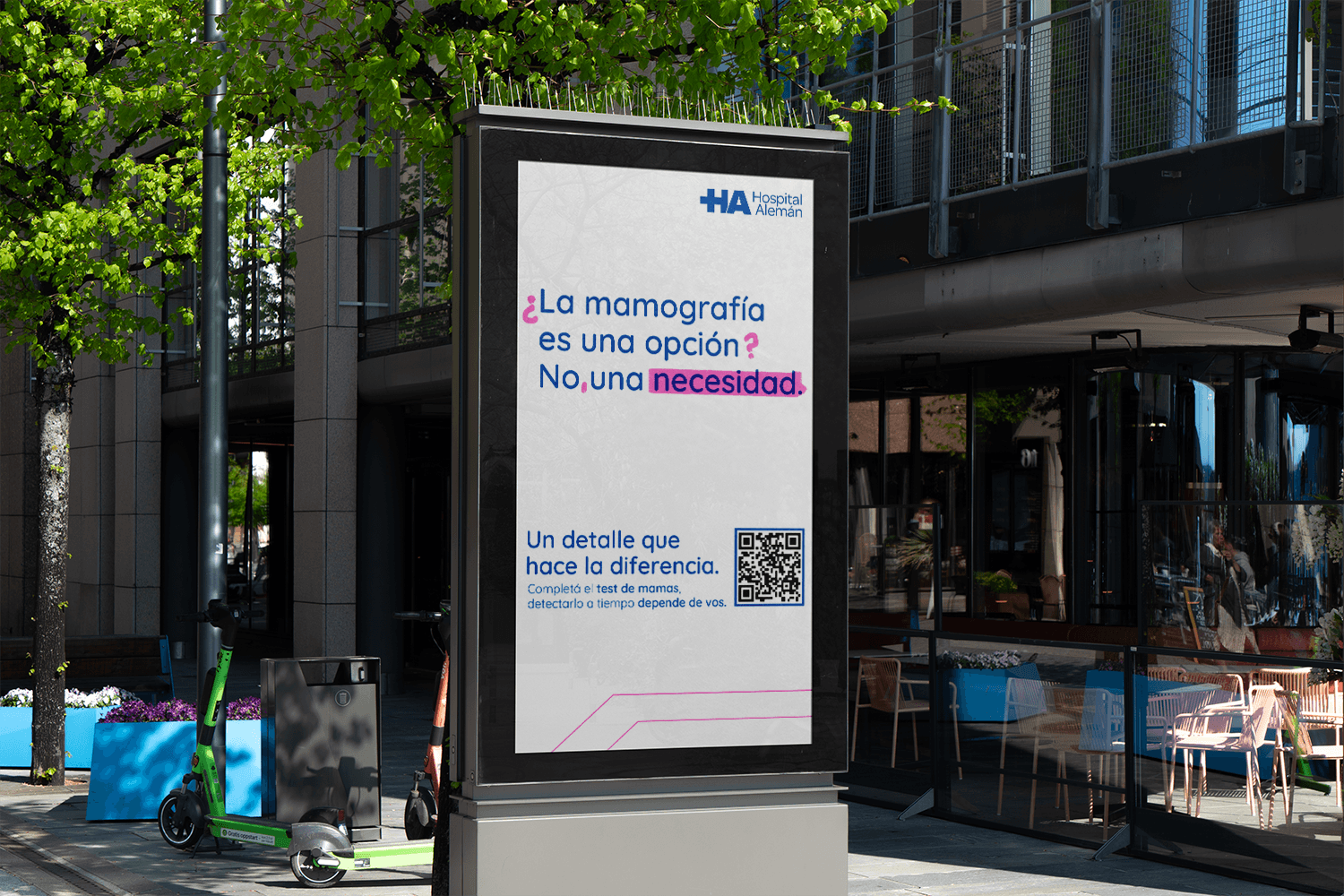 Outdoor illuminated lightbox display on a city sidewalk showing a white Hospital Alemán poster in Spanish stating that mammograms are a necessity, accompanied by a QR code.