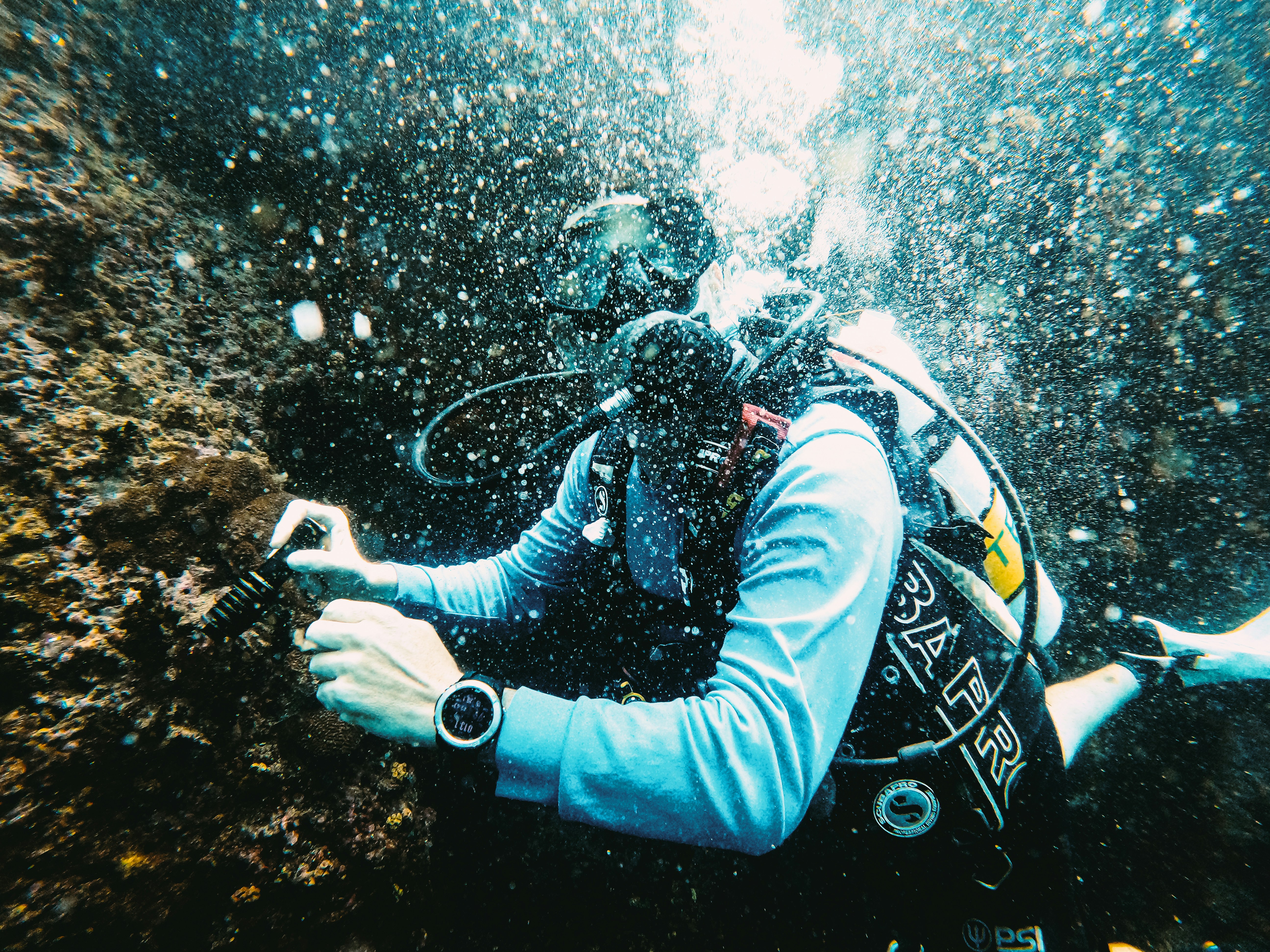 Scuba diver explores underwater rock formation with bubbles.