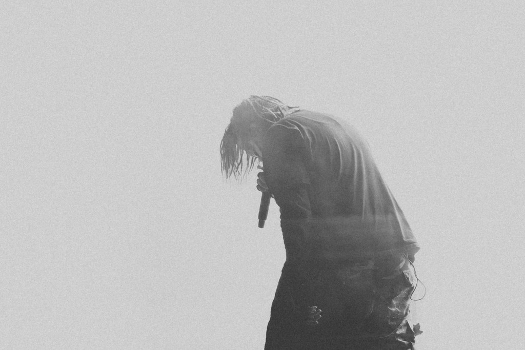 Black and white photo of a person with long hair holding a microphone, head bowed down.