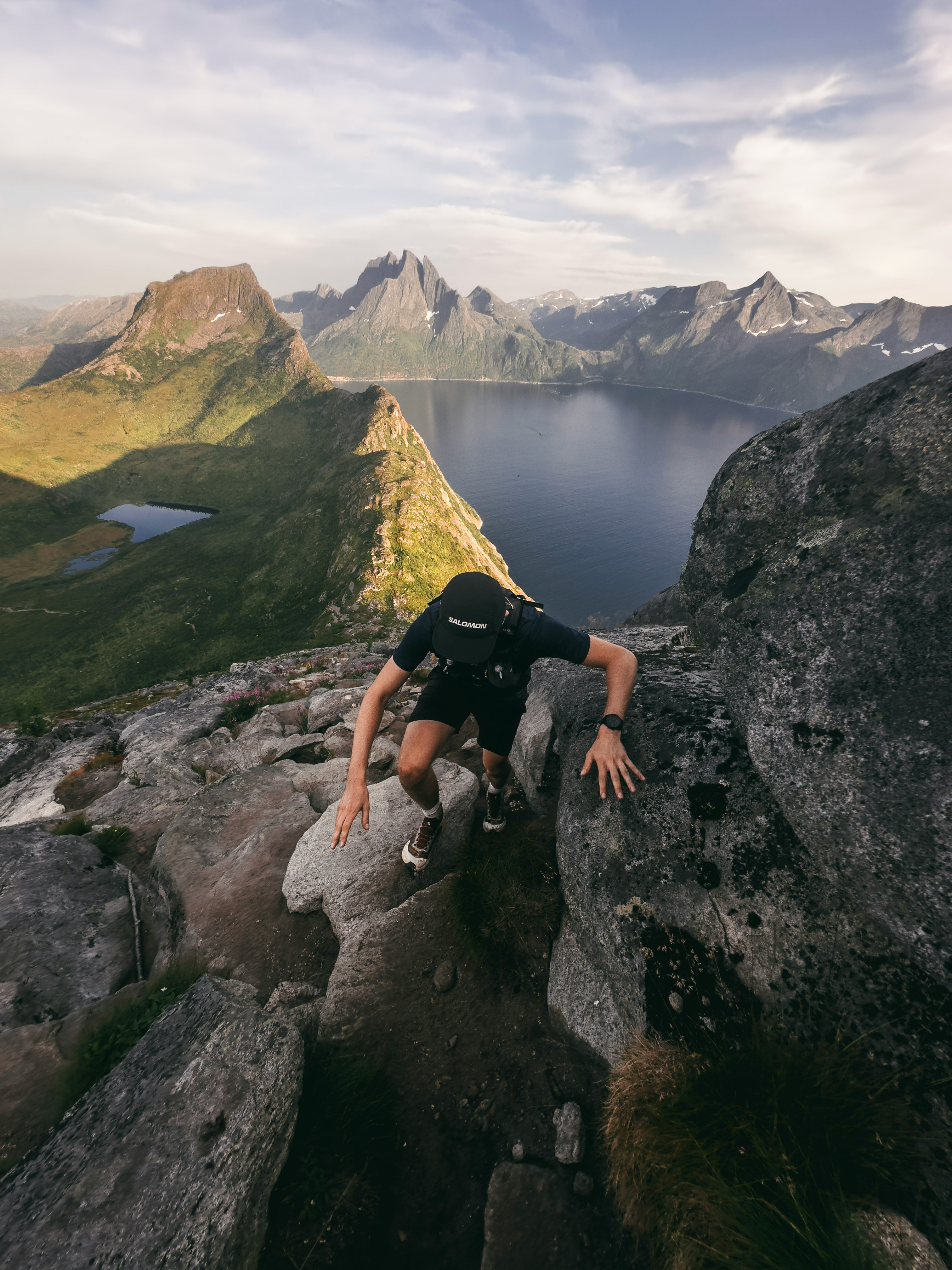 Man climbing a rocky mountain with a lake below.