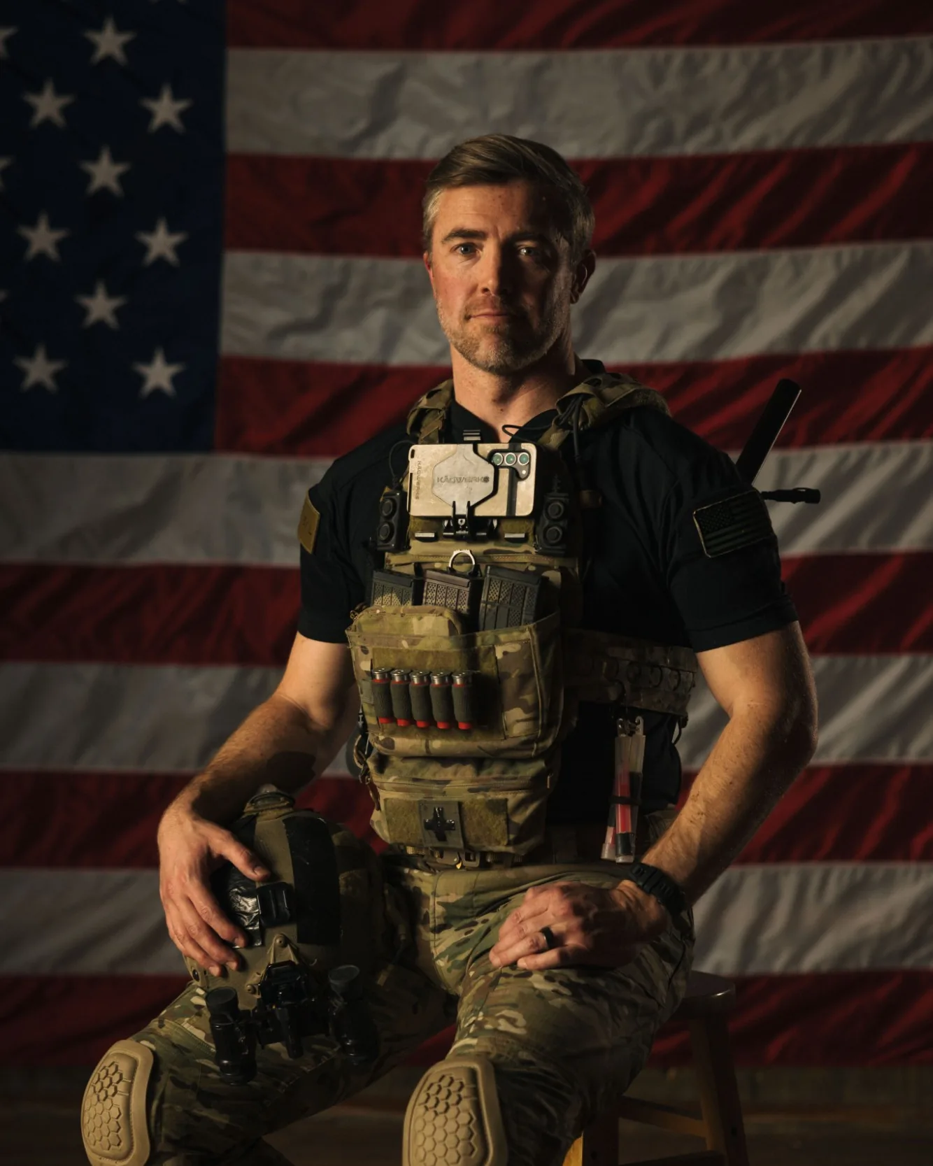 Reveal founder in plate carrier seated in front of an American flag